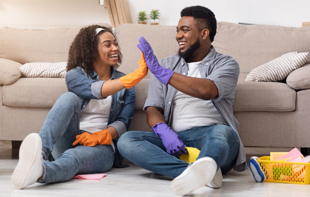 A couple sitting in front of their couch, high-fiving while cleaning their living room