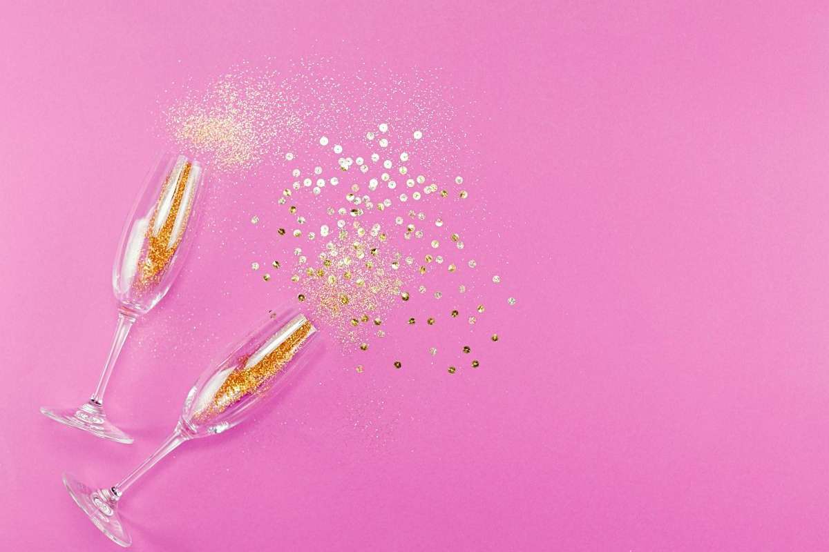 Spilled party glass full of gold glitter on pink background.