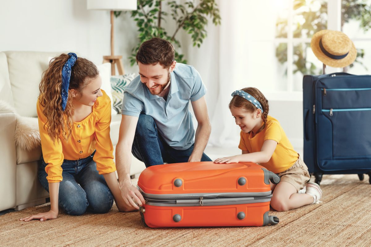 Smiling couple with little girl sitting on suitcase in living room ready before a holiday