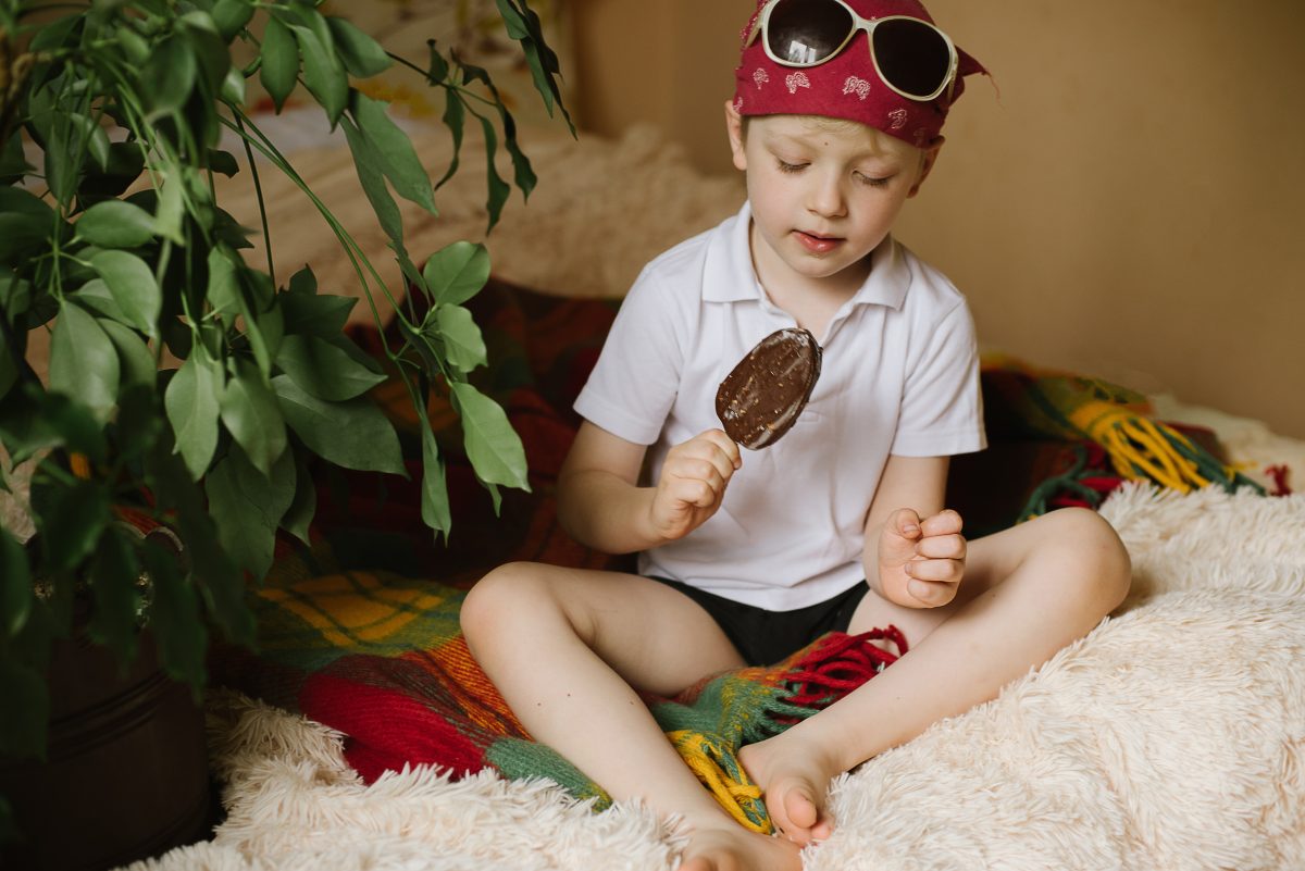 young boy wearing sunglasses eats chocolate ice-cream over a white carpet during summer