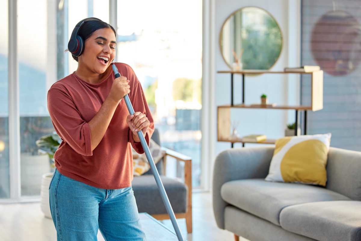 woman with headphones on cleaning her house and singing into the mop handle