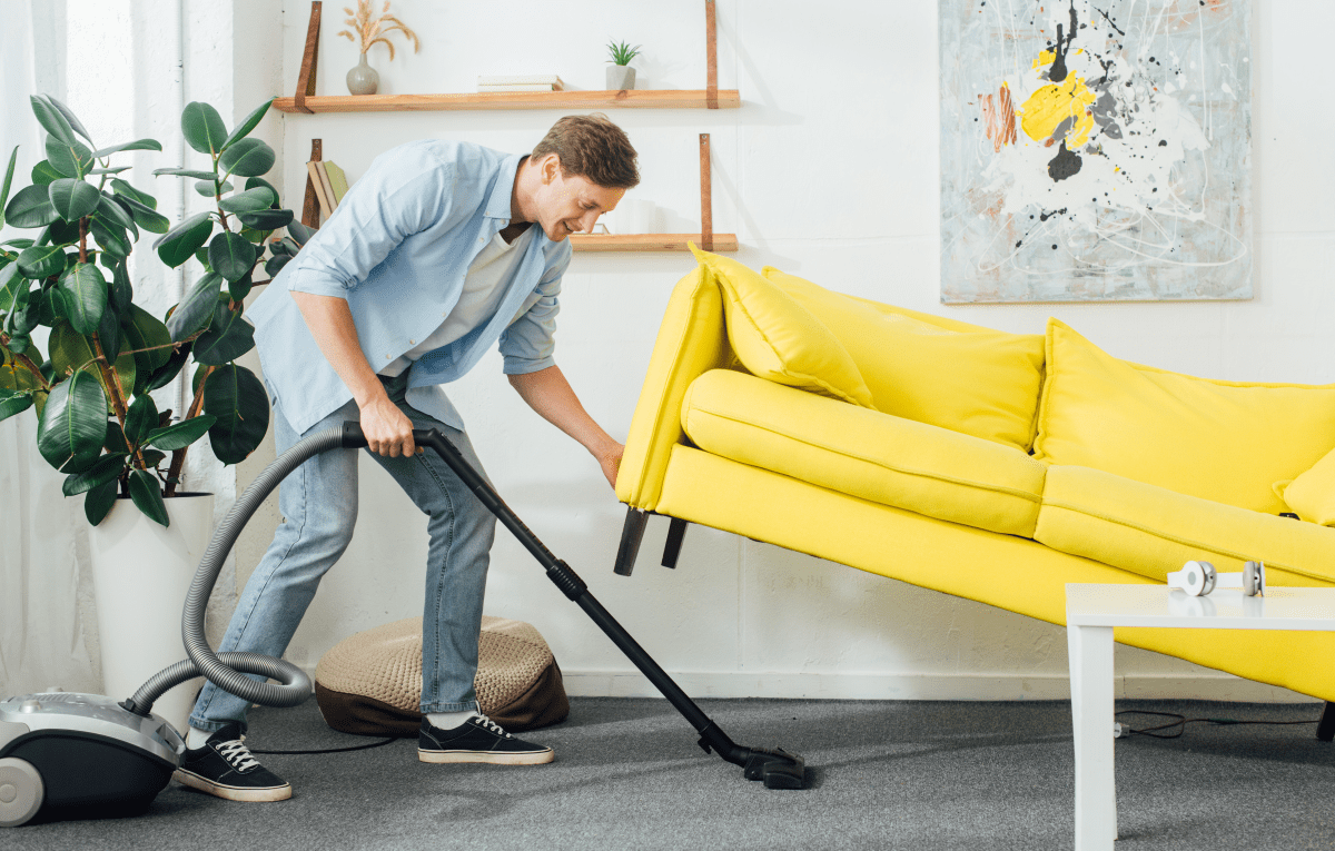Man holding up couch to vacuum underneath it